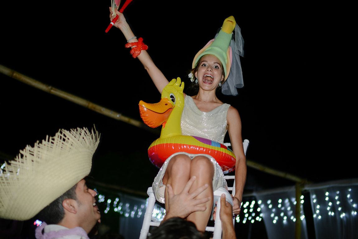 A guest in a party hat hoisted up on a chair, holding an inflatable duck