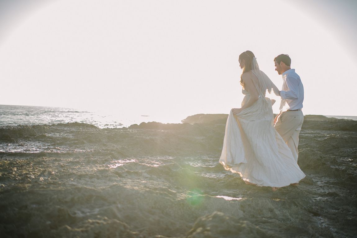 A couple on the rocks at the water’s edge at sunset