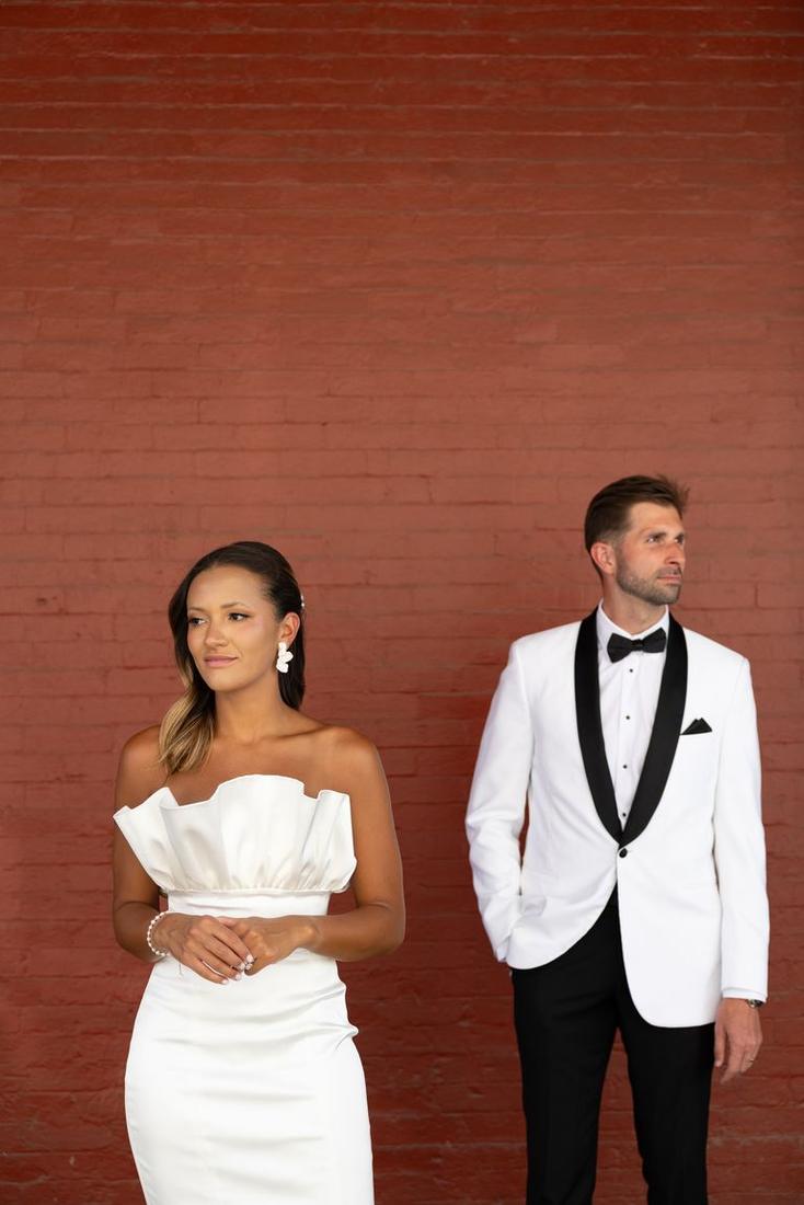 A couple in black and white formalwear against a brick wall