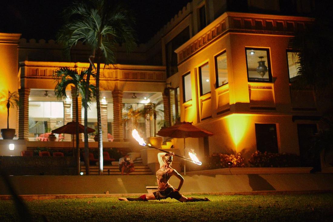 A fire dancer performing in front of a lit villa