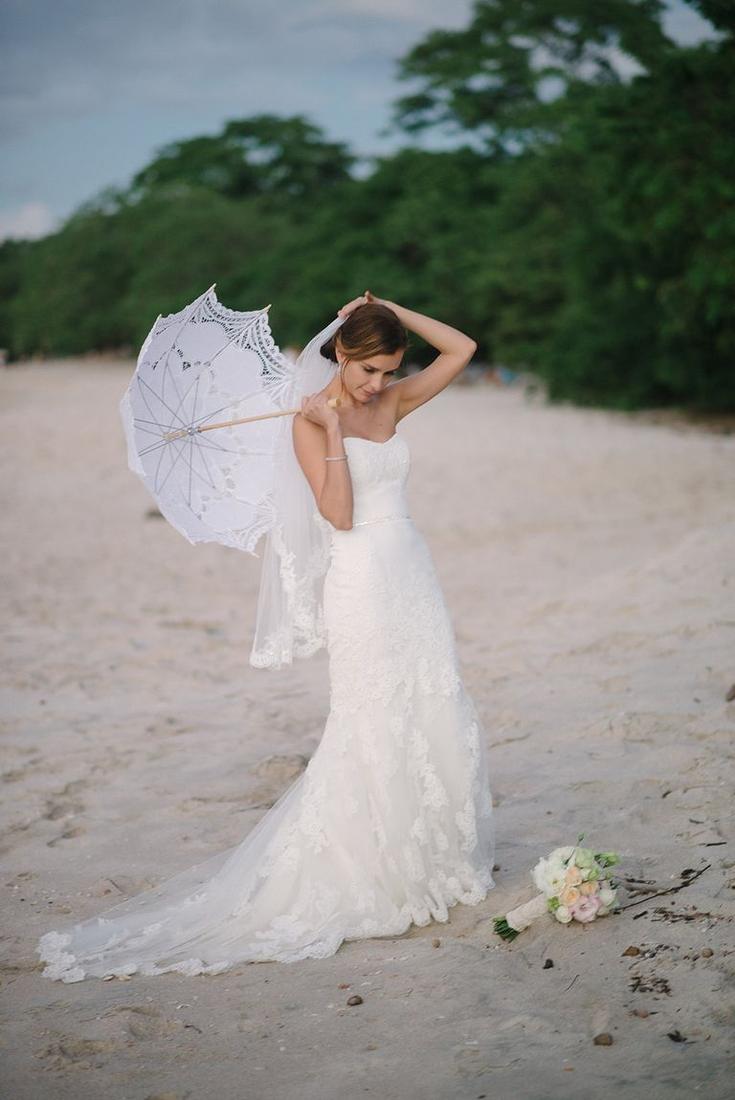 A bride on the beach holding a lace parasol