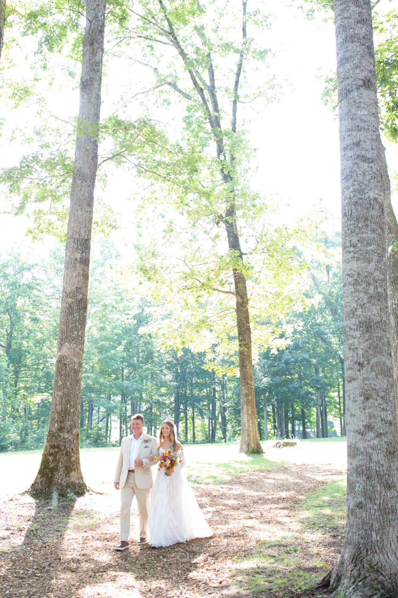 The bride and her father walking under tall trees