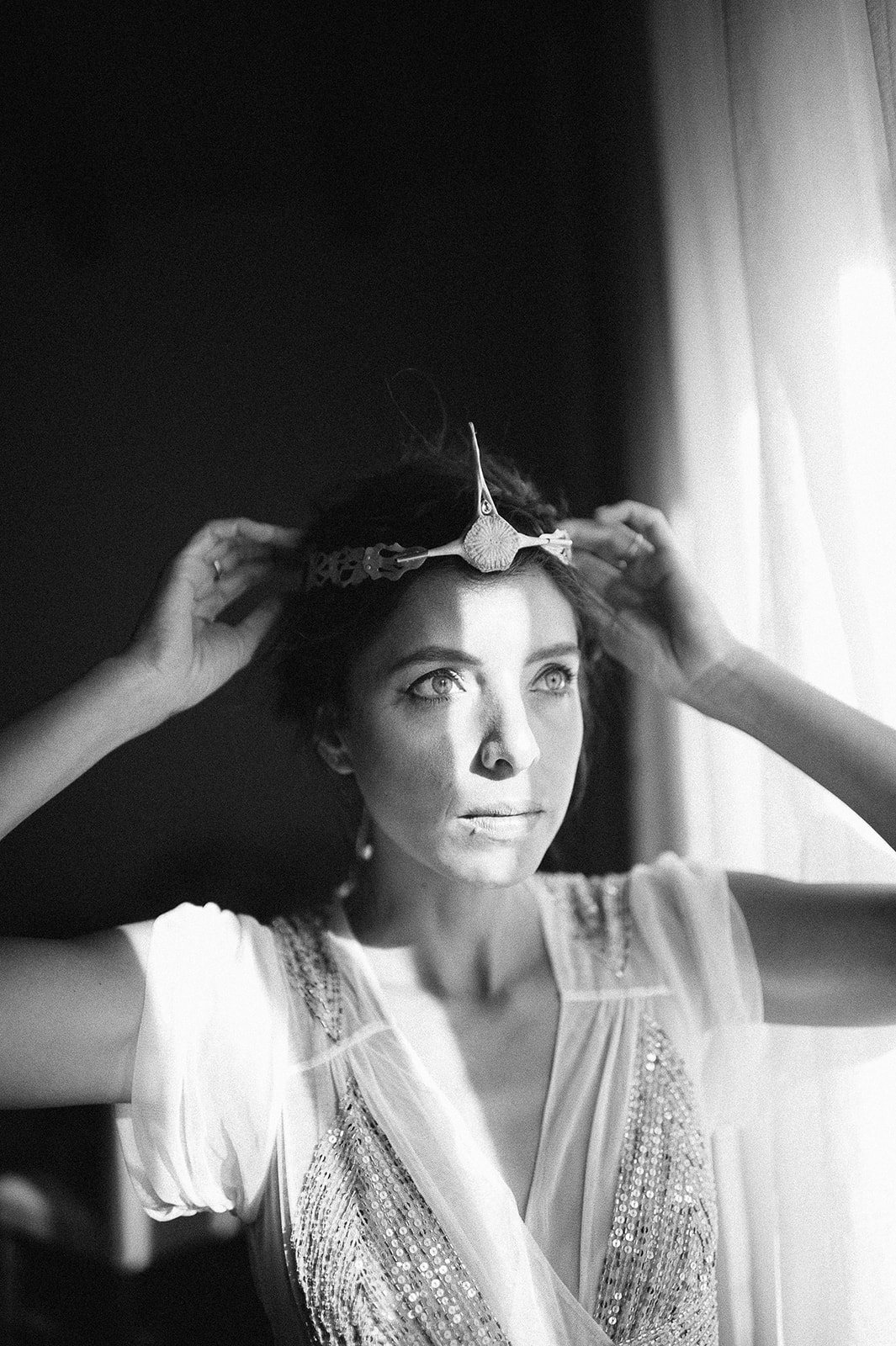 The bride fixing her headpiece, in black and white