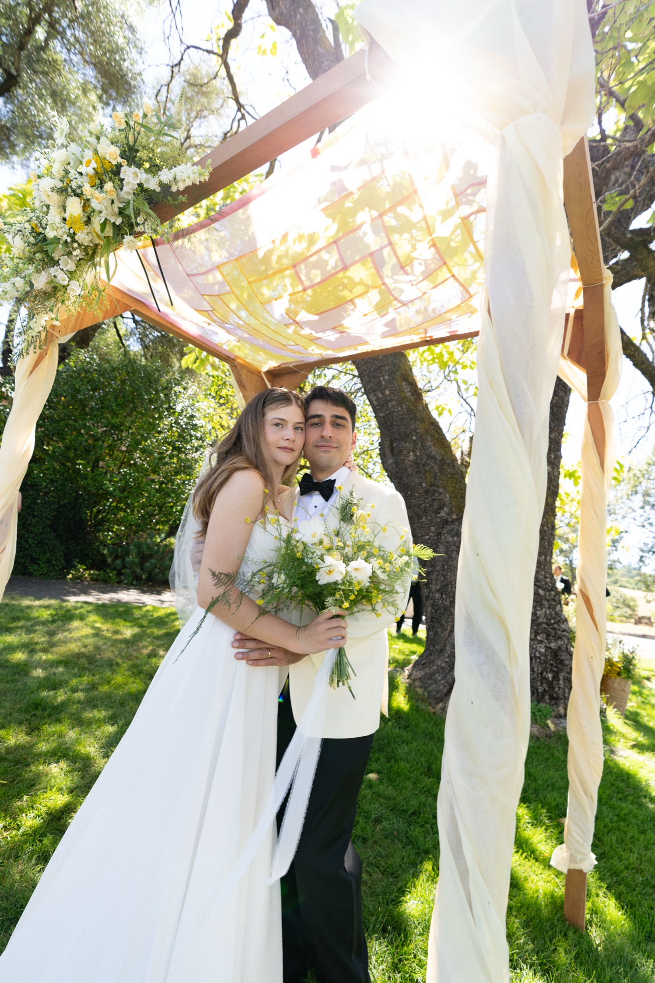 The couple framed by flowers, looking up into the sun