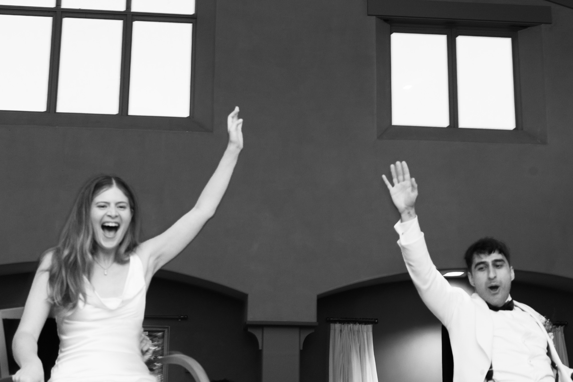 A bride and groom with their arms up in black and white