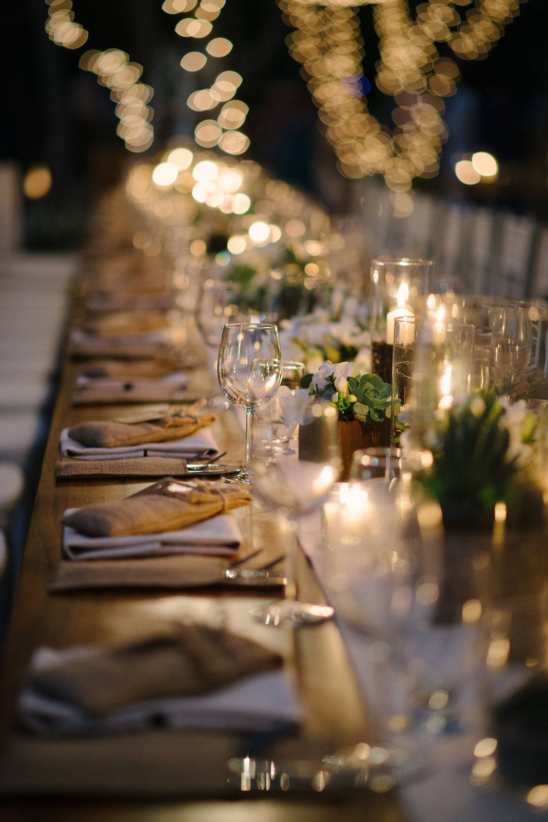 A long dinner table set with glassware and greenery
