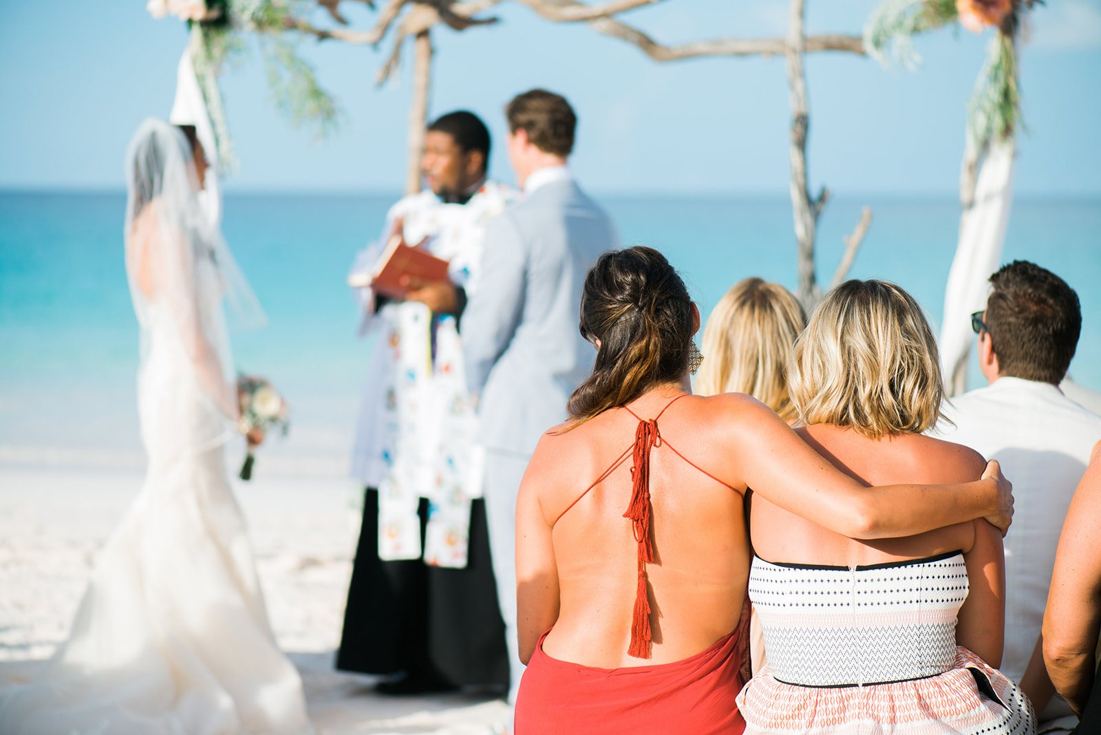 Guests with arms around each other at a beach ceremony