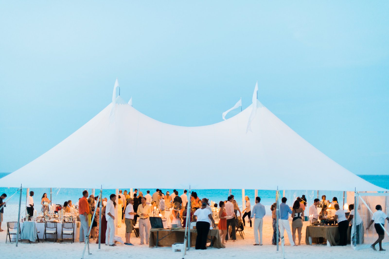 A white sailcloth tent full of guests on the beach at Harbour Island, the Bahamas