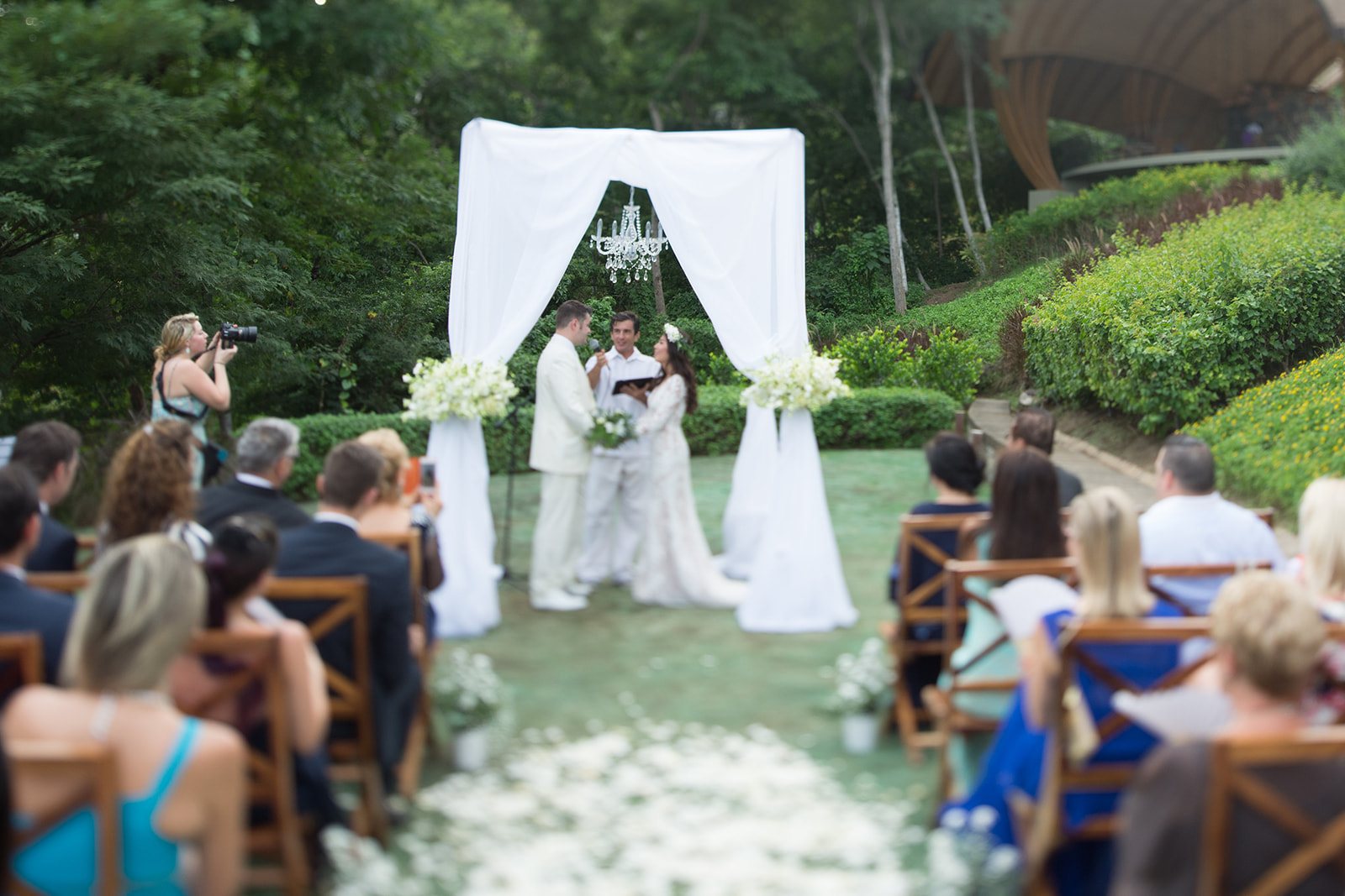 A ceremony under a white canopy, seen from the side